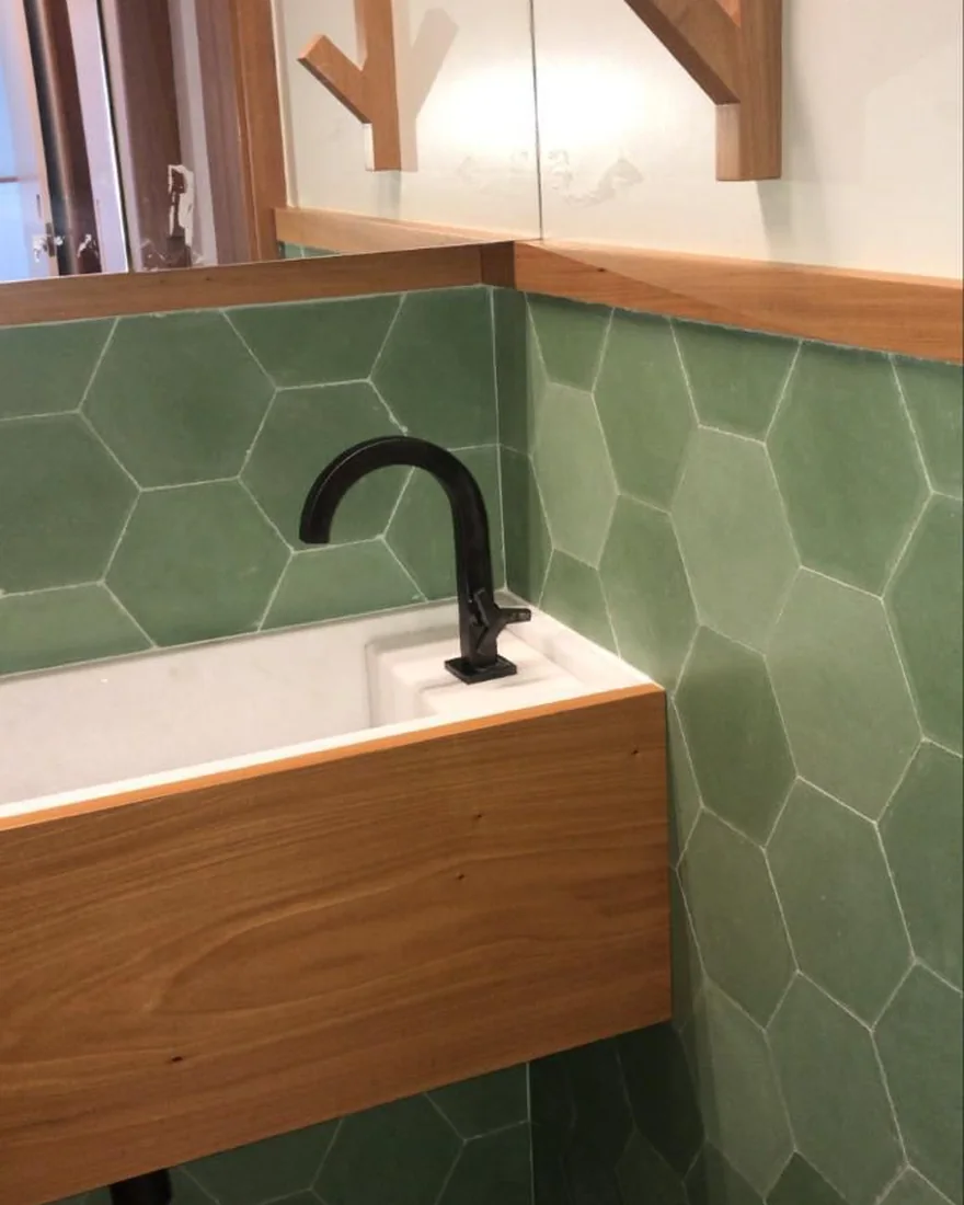Lavabo com revestimento hexagonal verde, bancada em madeira e metais pretos
